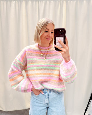 Model draagt een regenboog trui in pastelkleurtjes.