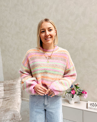 Model draagt een regenboog sweater in pastelkleurtjes.