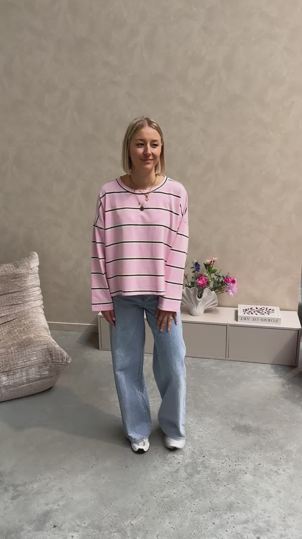 Model draagt een t-shirt met roze, bruine en witte streepjes op een rechte jeansbroek met stretch.