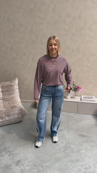 Model draagt een longsleeve met streepjes in roos en paars op een barrel jeansbroek met aan de zijkant een lichtere streep.
