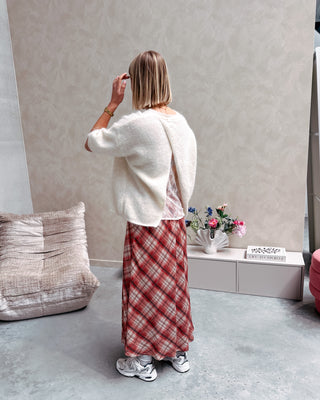 Model draagt een lange rok met ruitjes n oranje en wit, met daarop een witte trui met korte mouwen en achteraan kanten stof.