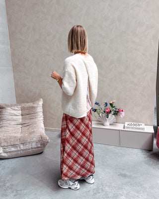 Model draagt een lange rok met ruitjes n oranje en wit, met daarop een witte trui met korte mouwen en achteraan kanten stof.