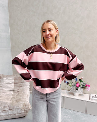 Model draagt een gestreepte sweater in de kleuren roos en bruin.