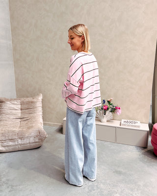 Model draagt een t-shirt met roze, bruine en witte streepjes op een rechte jeansbroek met stretch.
