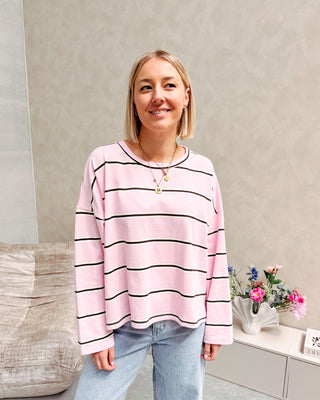 Model draagt een t-shirt met roze, bruine en witte streepjes op een rechte jeansbroek met stretch.