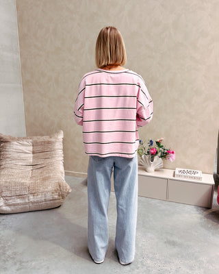 Model draagt een t-shirt met roze, bruine en witte streepjes op een rechte jeansbroek met stretch.