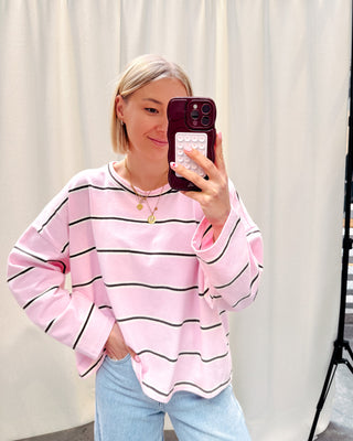 Model draagt een t-shirt met roze, bruine en witte streepjes op een rechte jeansbroek met stretch.