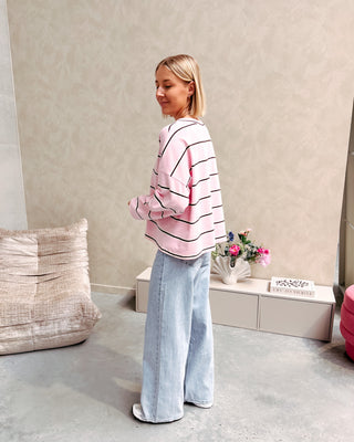 Model draagt een t-shirt met roze, bruine en witte streepjes op een rechte jeansbroek met stretch.