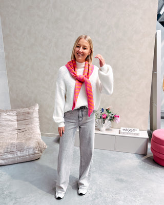 Model draagt een witte basic trui met daarop een driehoek sjaaltje met streepjes in felle kleurtjes, oranje en roze.