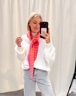 Model draagt een witte basic trui met daarop een driehoek sjaaltje met streepjes in felle kleurtjes, oranje en roze.