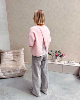 Model draagt een roze trui met korte mouwen en achteraan een kanten stof op een grijze rechte jeansbroek.