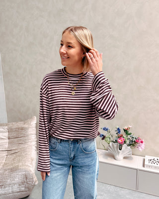 Model draagt een longsleeve met streepjes in roos en paars op een barrel jeansbroek met aan de zijkant een lichtere streep.