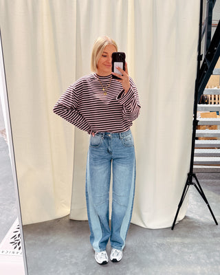 Model draagt een longsleeve met streepjes in roos en paars op een barrel jeansbroek met aan de zijkant een lichtere streep.