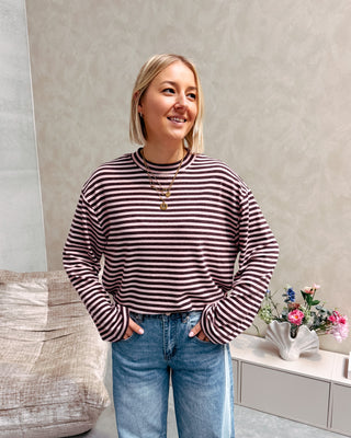 Model draagt een longsleeve met streepjes in roos en paars op een barrel jeansbroek met aan de zijkant een lichtere streep.