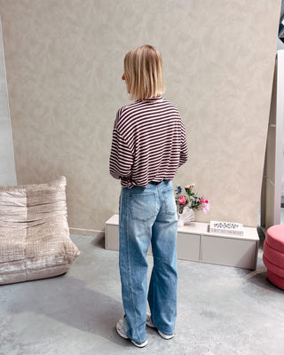 Model draagt een longsleeve met streepjes in roos en paars op een barrel jeansbroek met aan de zijkant een lichtere streep.