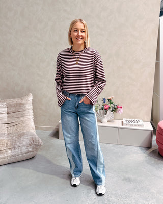 Model draagt een longsleeve met streepjes in roos en paars op een barrel jeansbroek met aan de zijkant een lichtere streep.