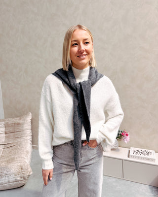 Model draagt een grijze jeansbroek met daarop een witte basic coltrui.