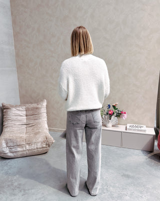 Model draagt een grijze jeansbroek met daarop een witte basic coltrui.