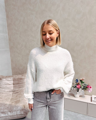 Model draagt een grijze jeansbroek met daarop een witte basic coltrui.