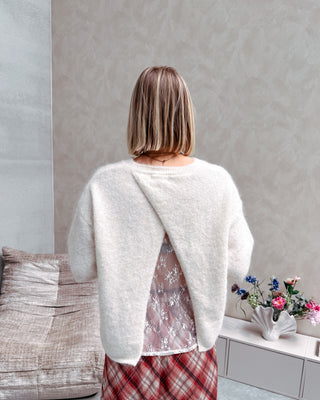 Model draagt een witte trui met korte mouwen en achteraan een kanten stof, op een lange rechte rok met ruitjespatroon.