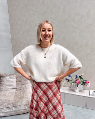 Model draagt een witte trui met korte mouwen en achteraan een kanten stof, op een lange rechte rok met ruitjespatroon.