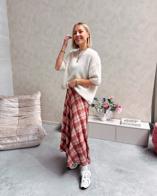 Model draagt een witte trui met korte mouwen en achteraan een kanten stof, op een lange rechte rok met ruitjespatroon.